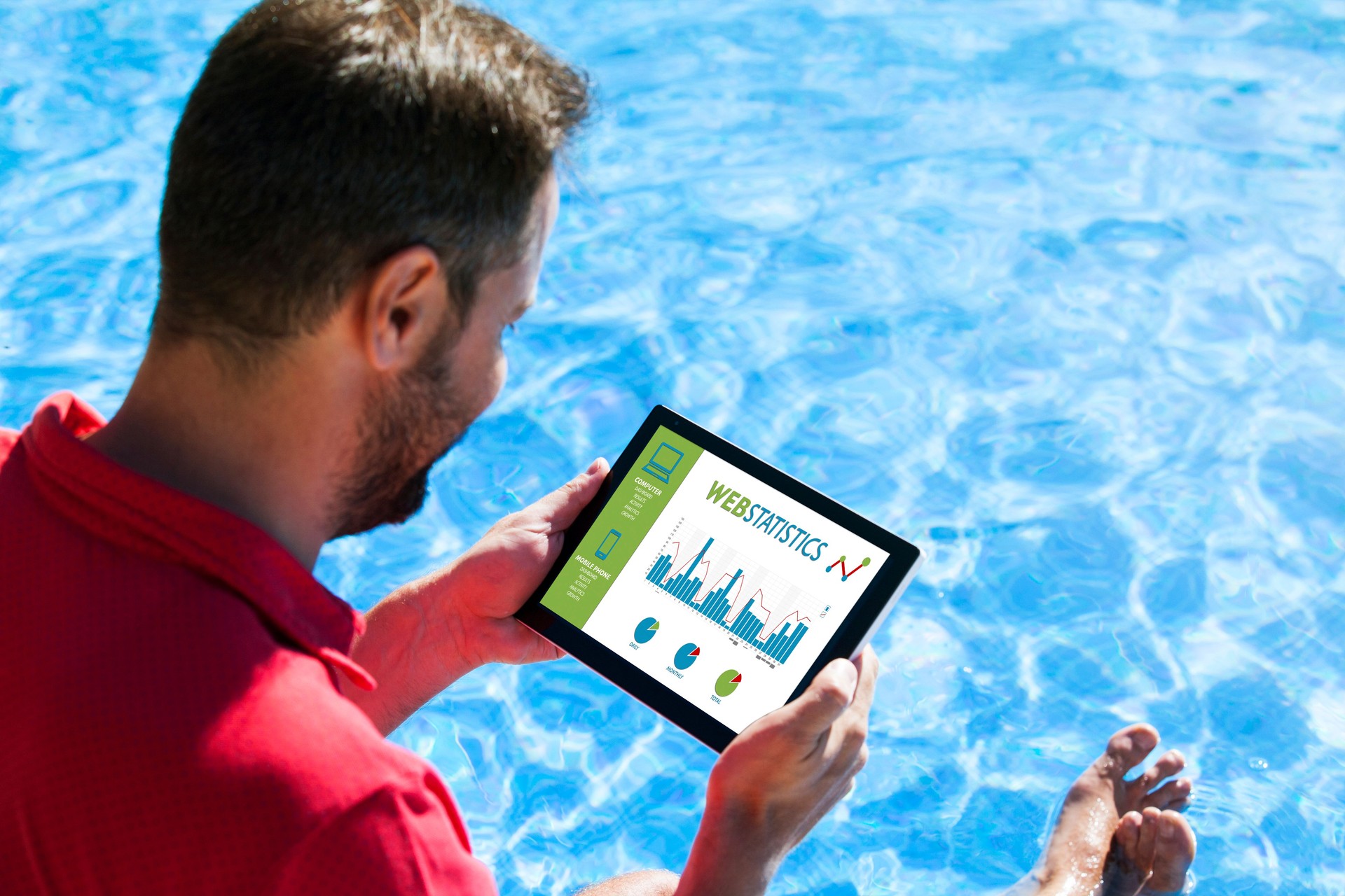 Man consulting web statistics with a tablet while sitting in the swimming pool edge.